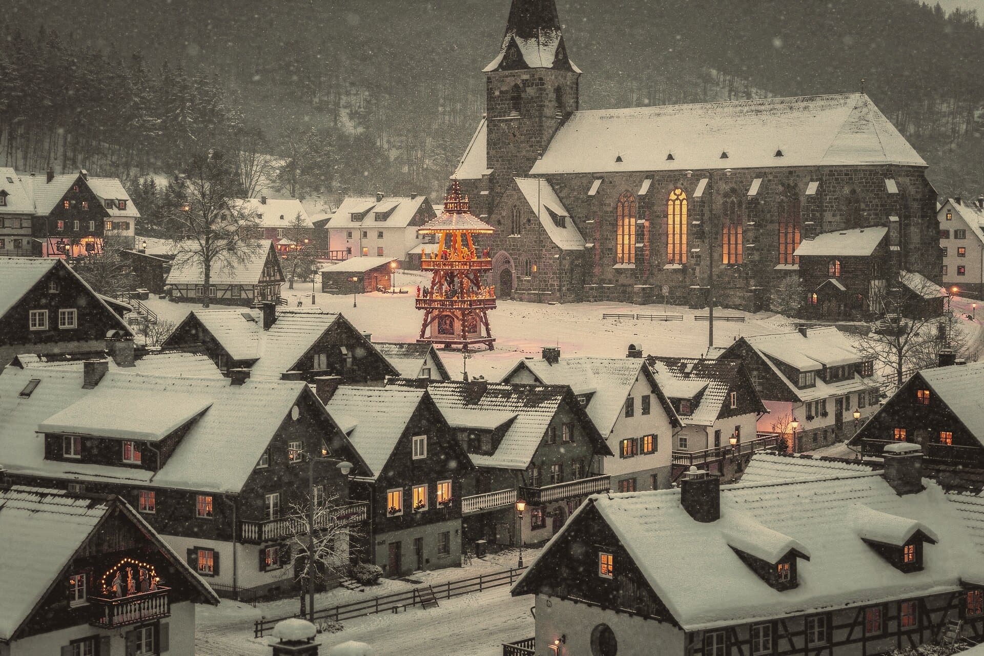A mining town at blue hour in deep snow: lit windows below a great Gothic church, a lit pyramid in the square.