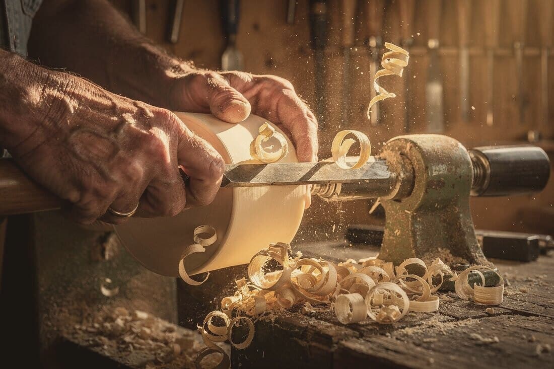 Hands guide a chisel against linden spinning on the lathe; shavings curl away.