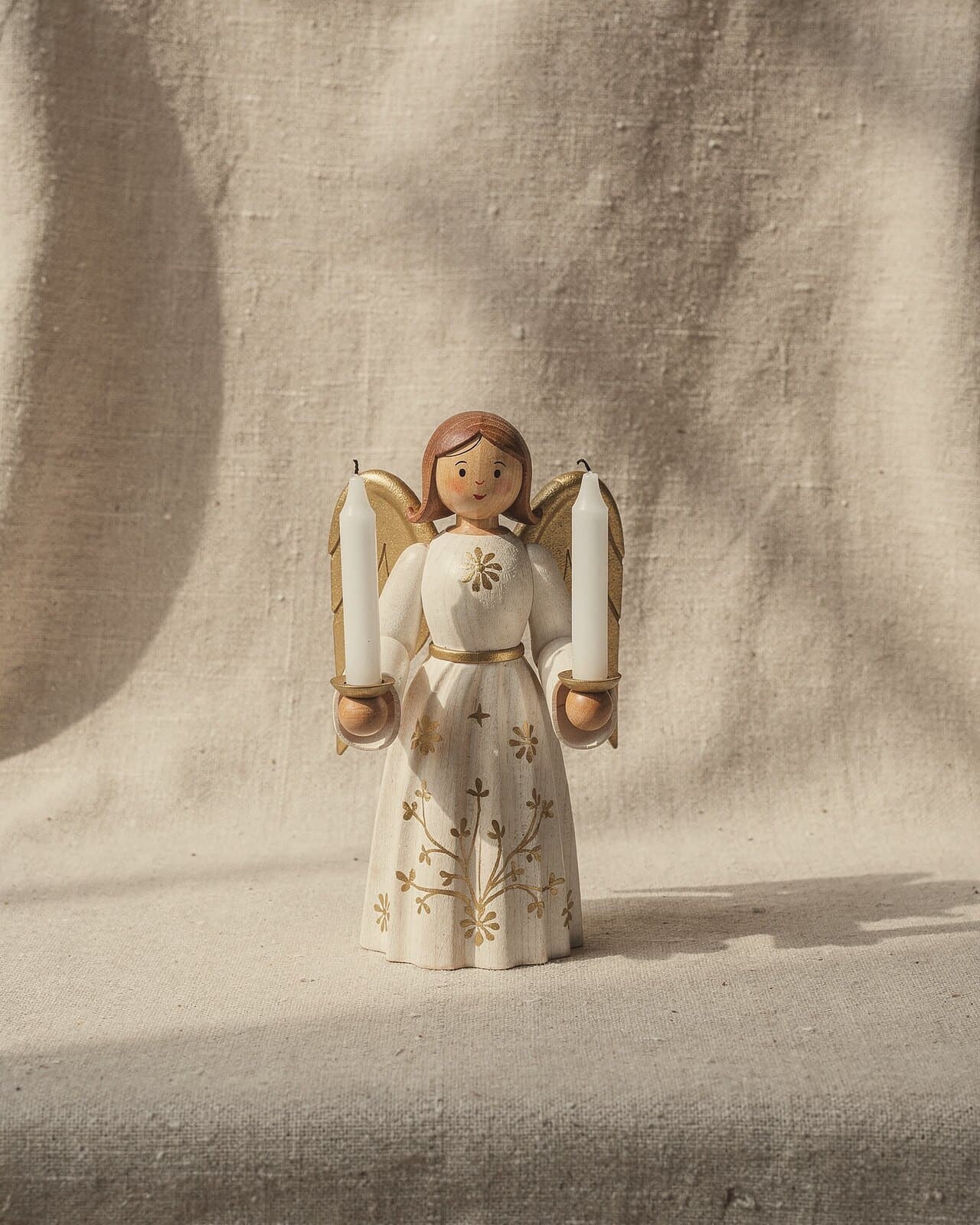 A light-bearing angel in a white robe with gold patterns and gold-tipped wings, a candle in each hand.