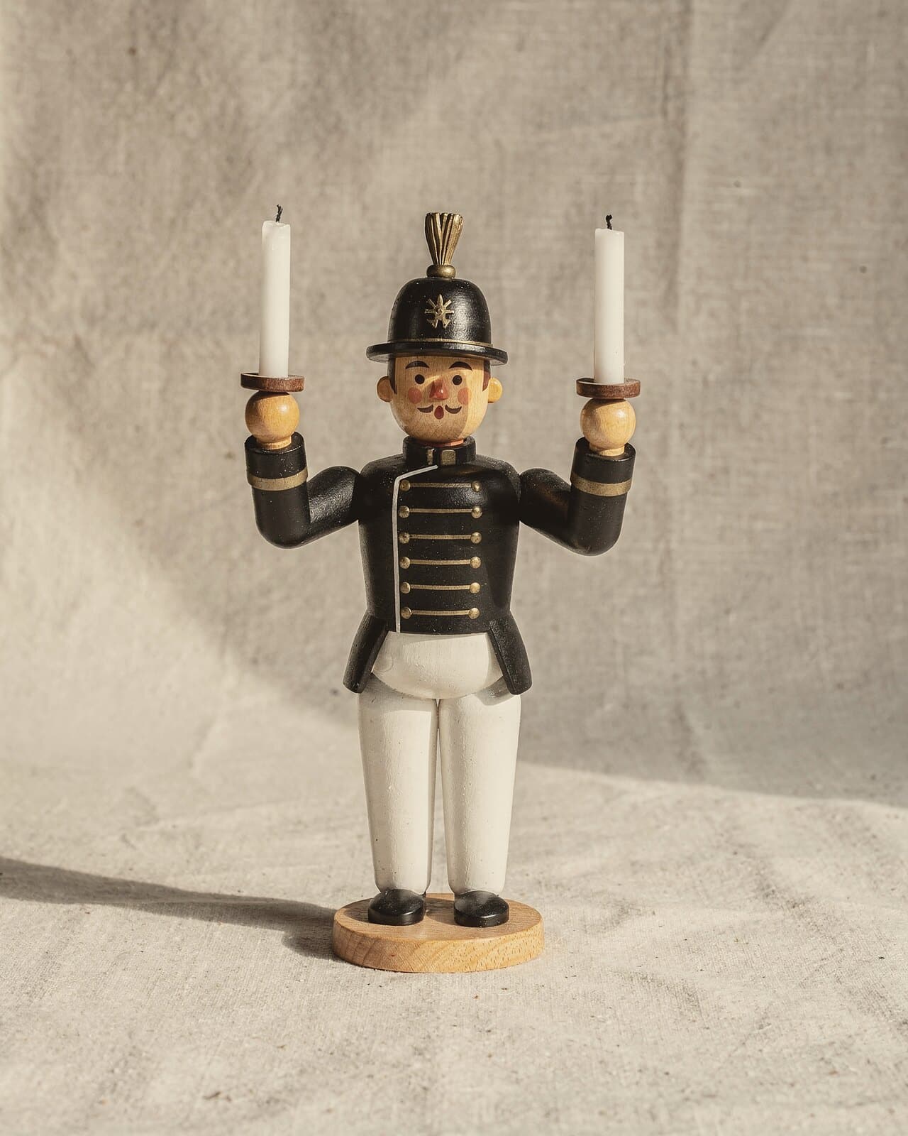 Ein Lichterbergmann im schwarzen Habit mit weißer Hose und Federbusch, in jeder erhobenen Hand eine Kerze.