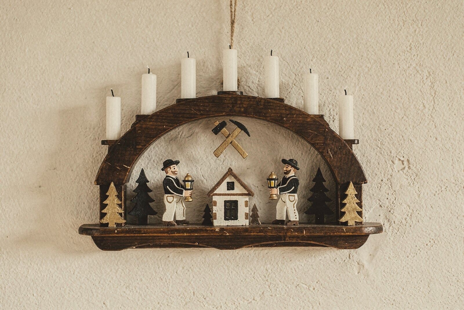 Ein dunkler Bergmannsbogen mit sieben Kerzen: zwei Bergleute mit Lampen, Schlägel und Eisen, ein Huthaus und Fichten.