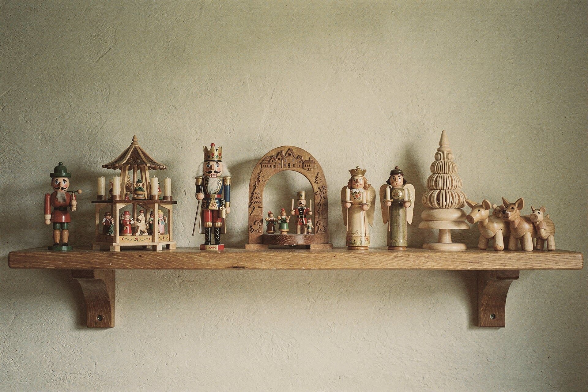 The seven kinds side by side on a wall shelf: a smoker, a pyramid, a nutcracker, a candle arch, an angel and a miner, a shaved tree and ring-turned animals.
