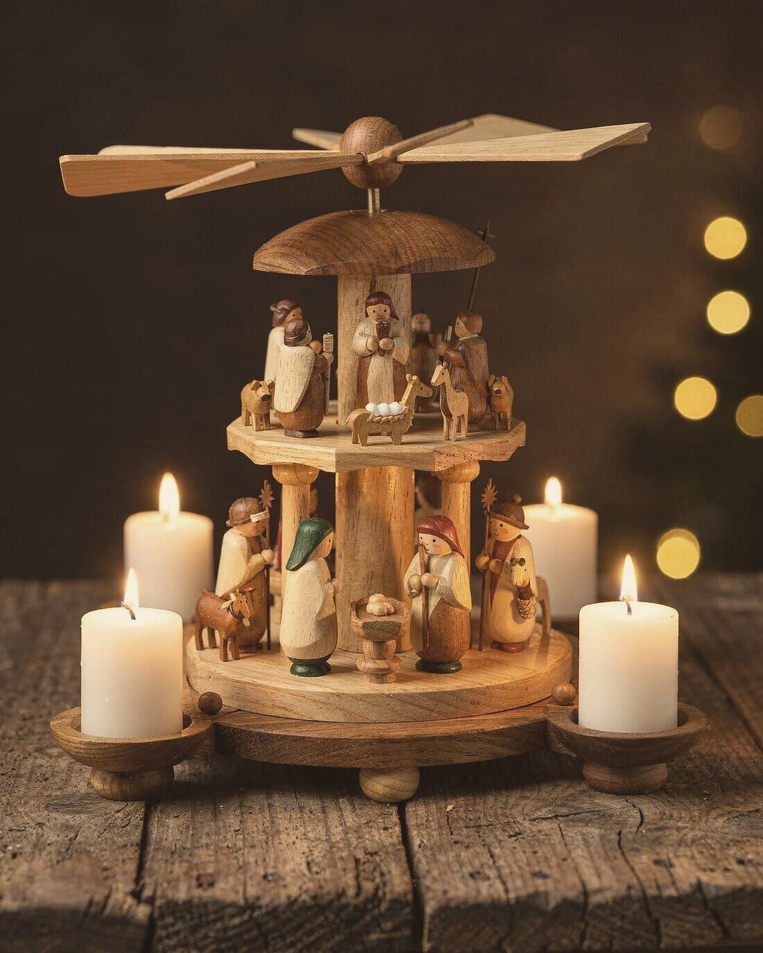 A three-tier nativity pyramid with lit candles and a vane wheel on top.