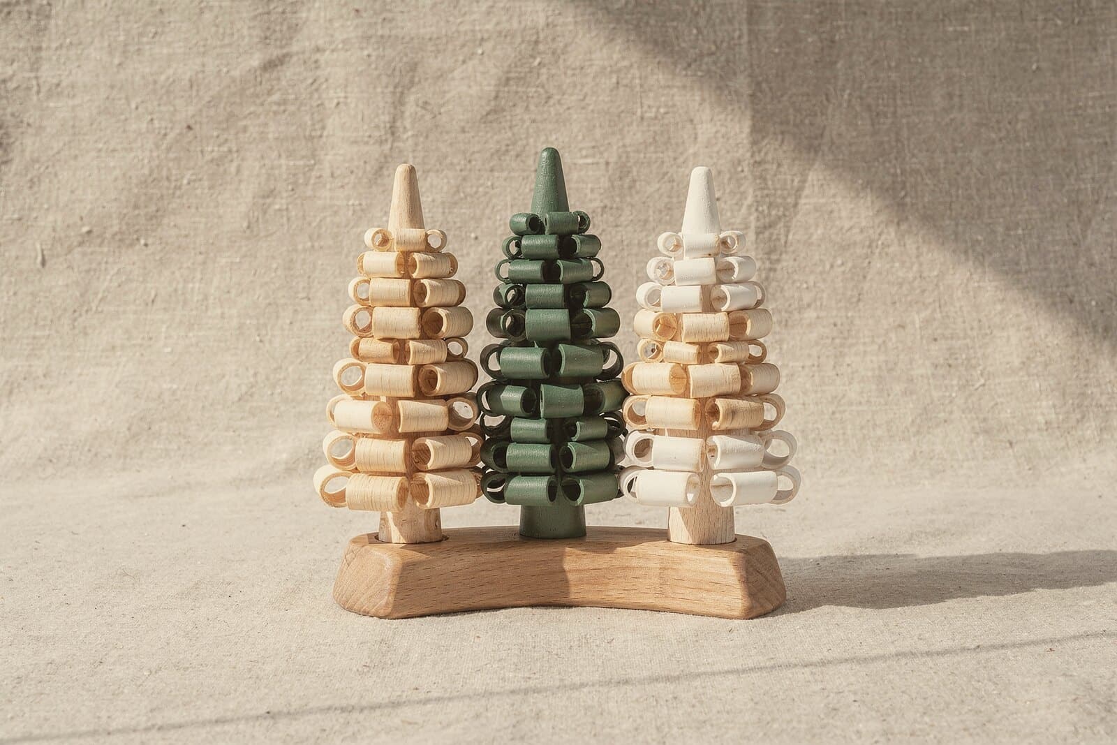 Three small shaved trees on one base: natural pale wood, soft green, and white-tipped like fresh snow.