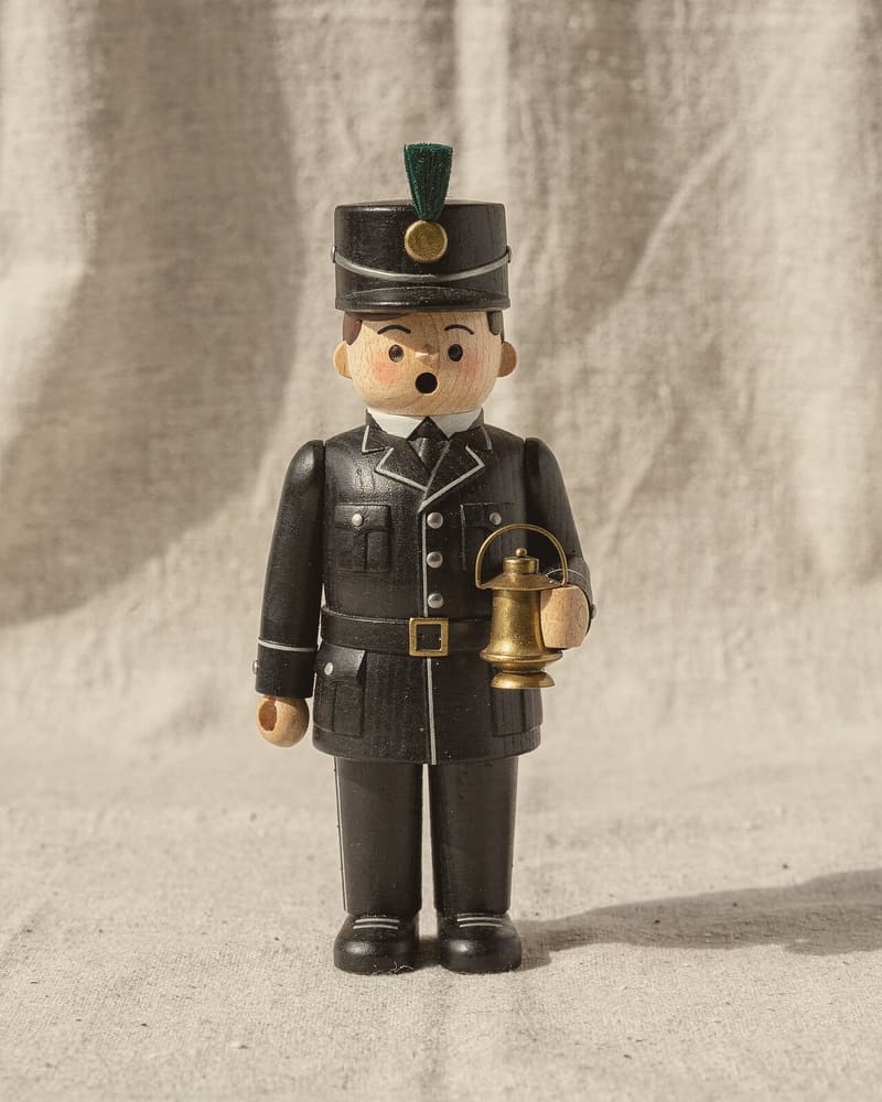 A wooden smoker in the shape of a miner in black uniform and peaked cap, holding a brass lamp, his round mouth open.